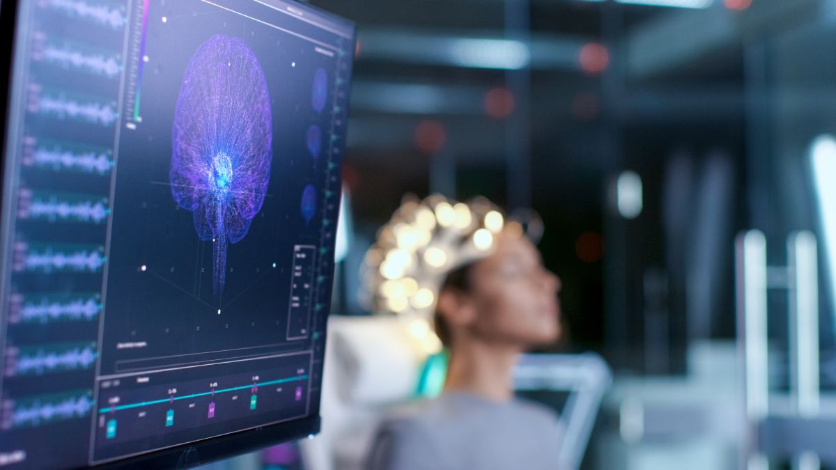 Woman in blurred focus sits connected to an EEG machine getting a brain scan